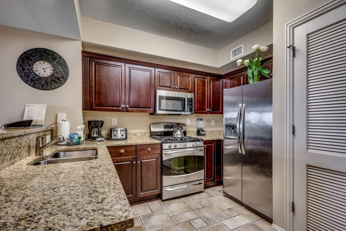 A cozy, functional kitchen featuring granite countertops, stainless steel appliances, and dark wood cabinets. The space is tidy and well-stocked, signaling a home equipped for both short and extended stays.