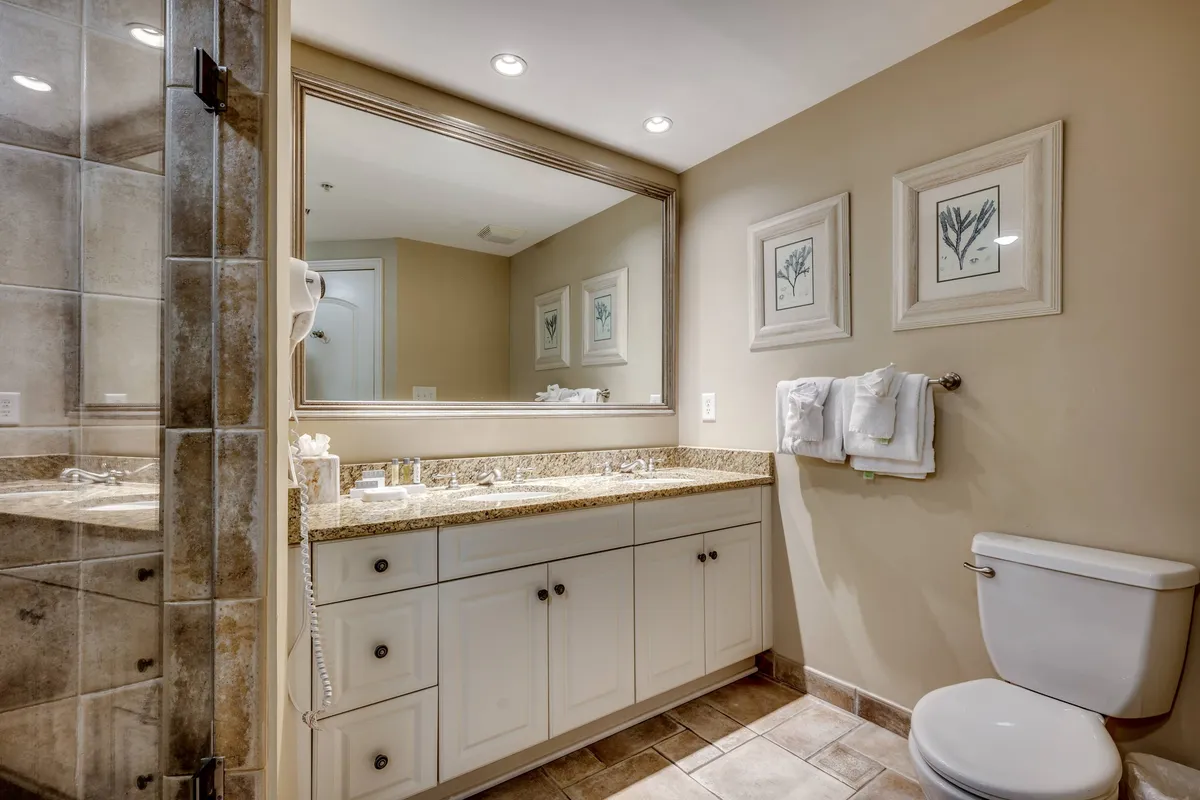 A bright and inviting bathroom vanity area featuring a spacious countertop, a large mirror, and plush white towels neatly arranged. Framed artwork and modern lighting add a touch of elegance, while the visible towels reinforce the sense of thoughtful amenities.