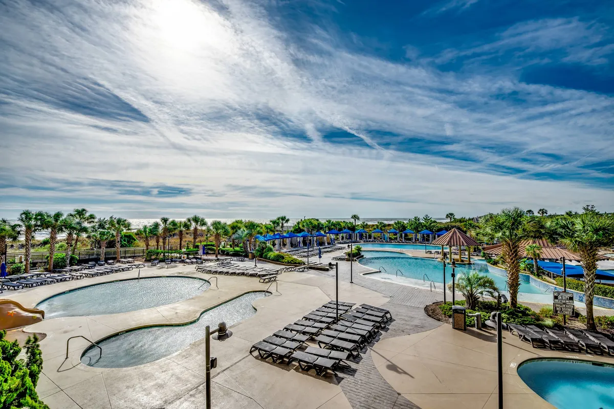 This image depicts an inviting resort-style pool area surrounded by palm trees, lounge chairs, and a cabana area. The setup is ideal for family relaxation, sunbathing, and socializing, evoking the vibrancy and leisure of a fun-filled vacation setting.