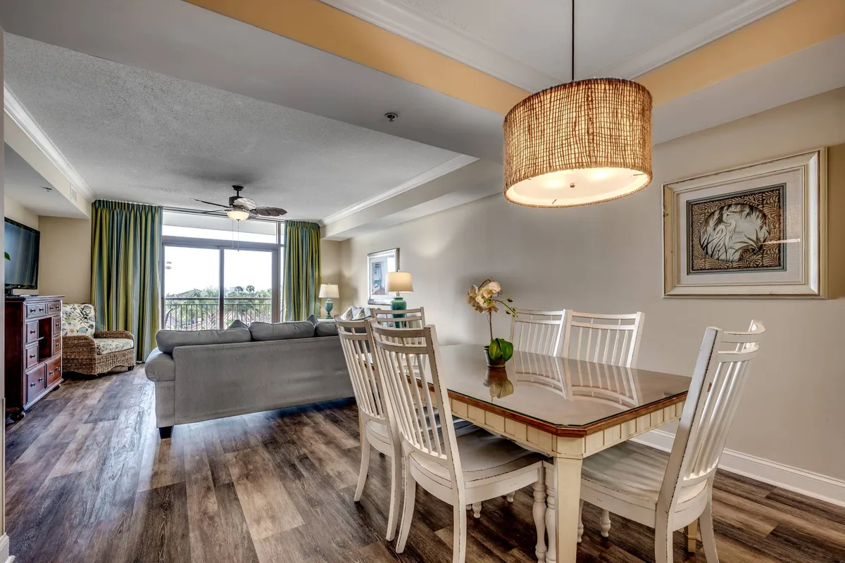 A view of the dining area and living space with a large window allowing sunlight to flood the room. The inviting dining table and cozy living area emphasize a comfortable and sociable atmosphere, while the natural light accentuates the openness of the interior.