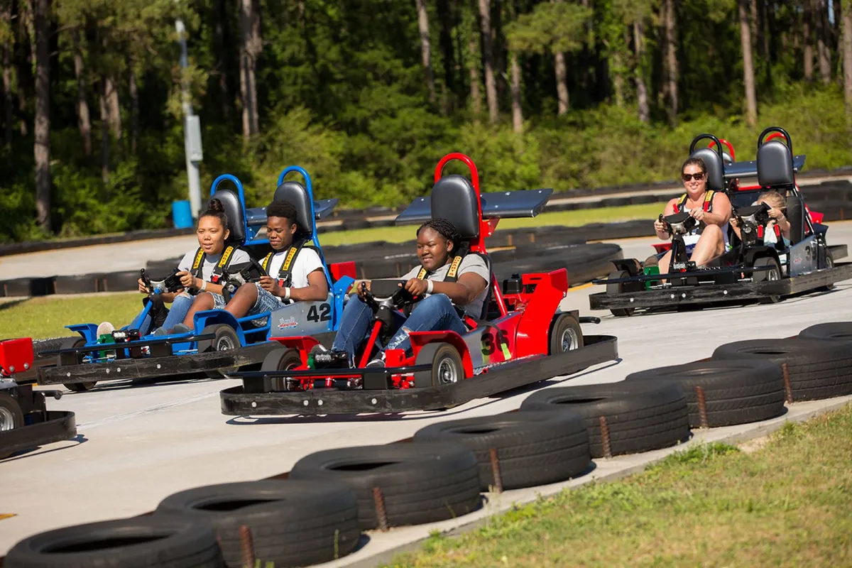 A dynamic go-kart track scene featuring several participants in action, surrounded by trees. The joyful atmosphere and presence of families and groups capture the thrill and excitement of local attractions suitable for all ages.