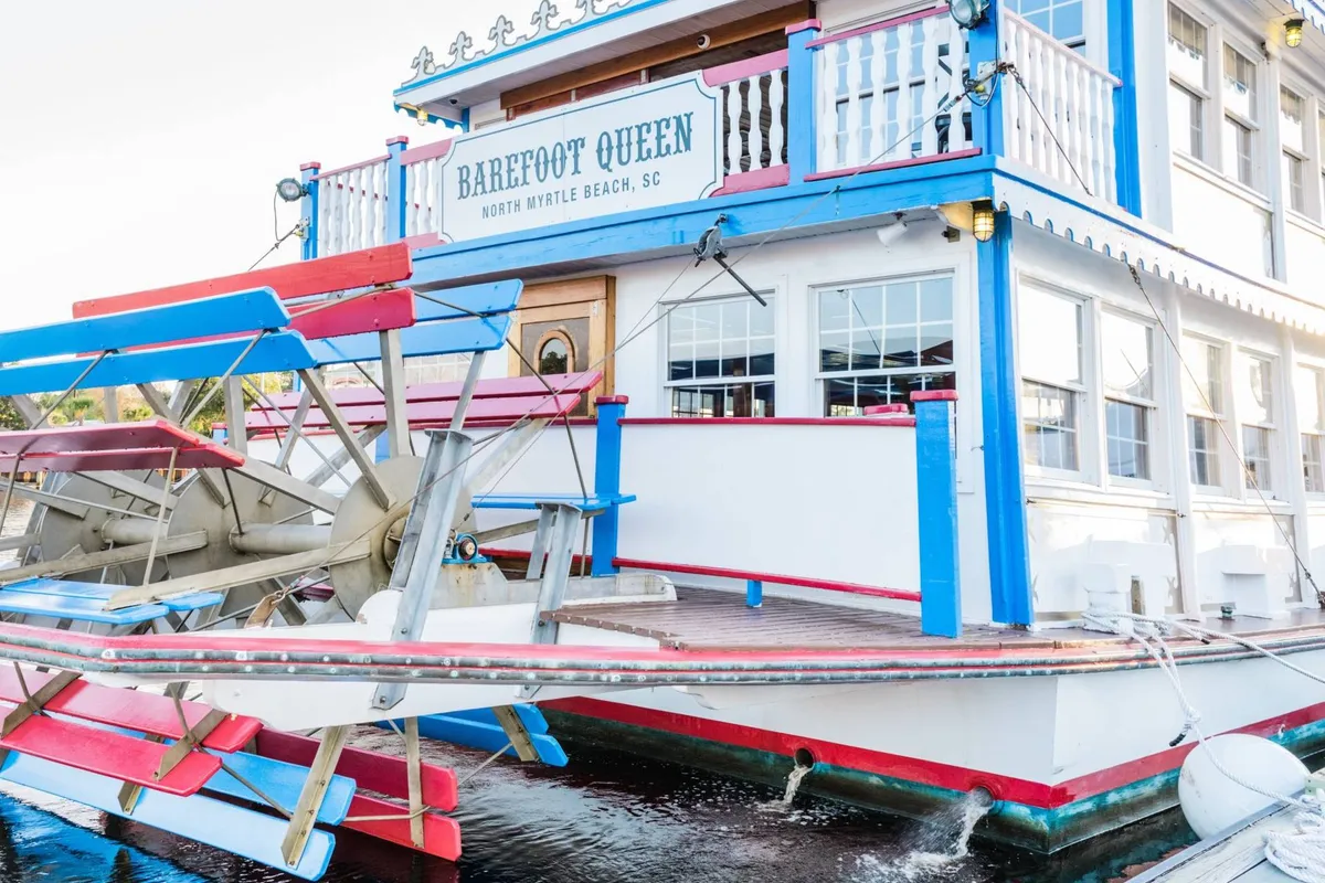 A brightly colored paddle wheel riverboat with playful signage, docked and ready for sightseeing or dining cruises. The festive mood and unique structure promise a memorable out-of-the-ordinary family adventure on the water.