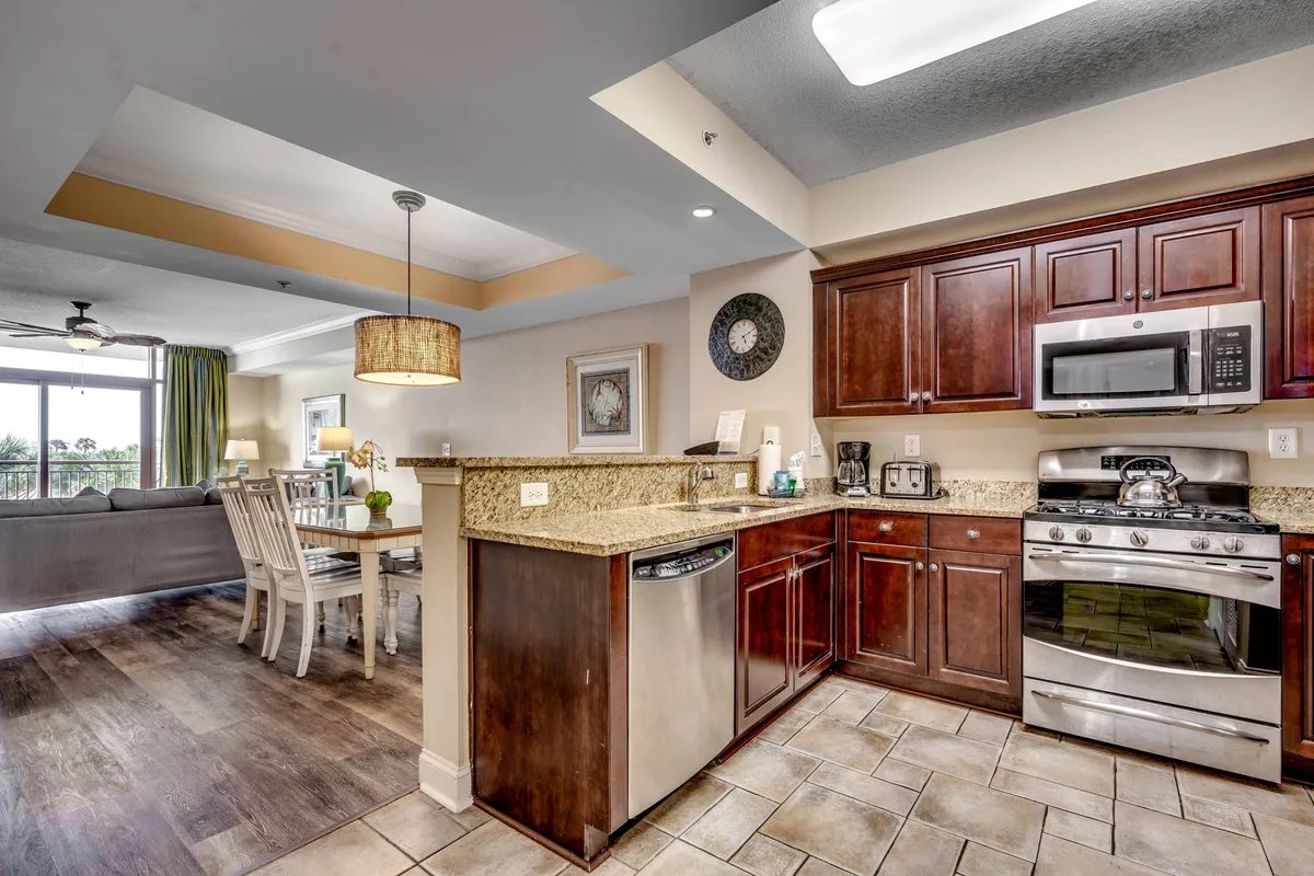 This image presents an open-concept living space that seamlessly merges the kitchen equipped with granite countertops and stainless steel appliances, a dining area, and a portion of the living area. The abundant natural light and thoughtful layout exemplify a central gathering hub ideal for cooking, dining, and relaxing together.