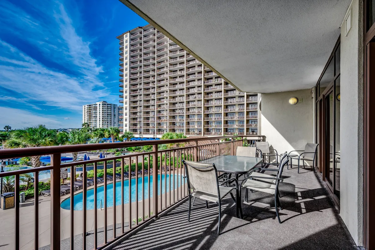 This image captures a stylish oceanfront balcony furnished for relaxation, with views overlooking the swimming pool and high-rise building against a brilliant blue sky. The atmosphere is tranquil, ideal for group conversations or enjoying morning coffee while taking in coastal vistas.